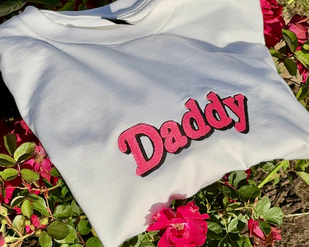 White shirt with 'Daddy' printed in red on a background of pink flowers and green foliage